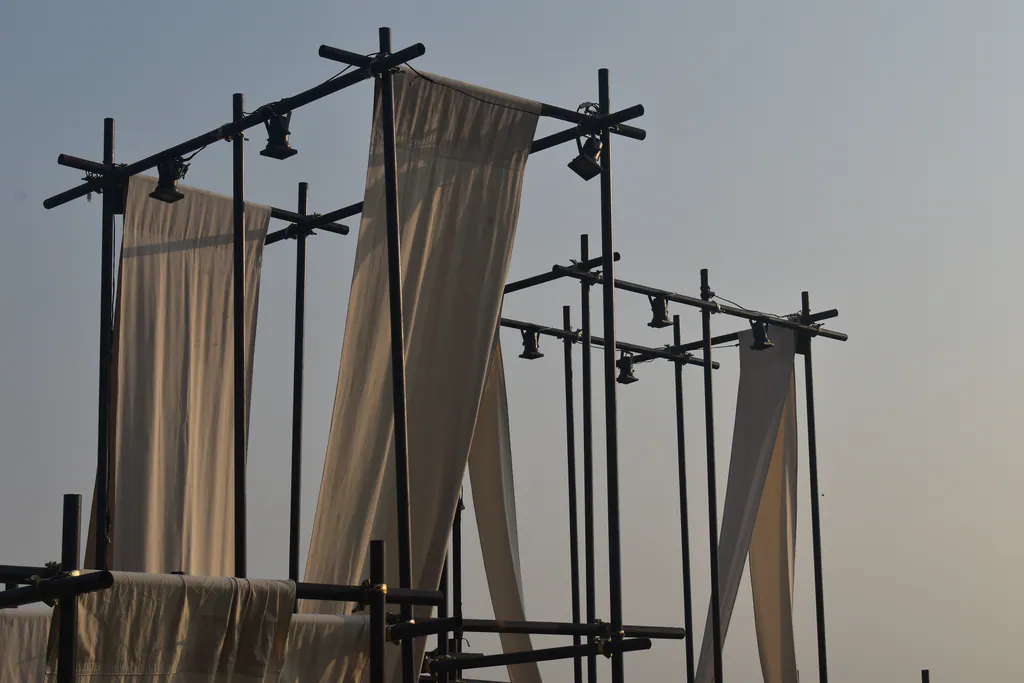 The Spot by day: black scaffold frames with lamps and long drapes of cream fabric against a pale sky