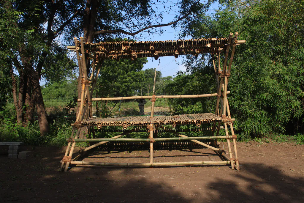 The X, finished: a two-level bamboo seat of crossed members under trees, on a bare earth clearing
